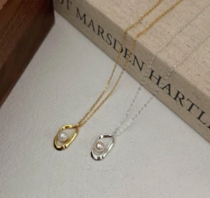 Necklace in sterling silver 925 with an irregular/organic open teardrop-shaped pendant, embracing a loose pearl at the centre. A minimalist, contemporary design, with a polished finish, available in gold or silver tone — a versatile piece for everyday wear or more elegant looks.